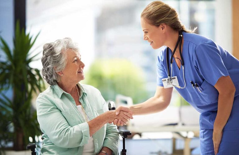 Nurse reviewing medications with an older resident at a bright assisted living dining table.