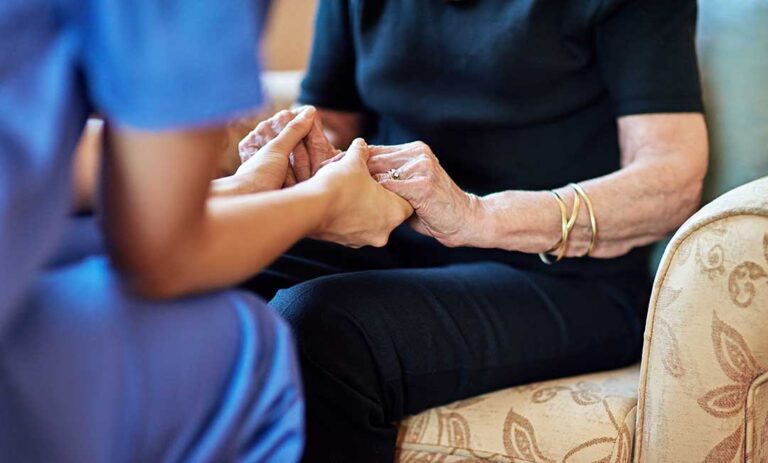 Older adults participate in a seated exercise class with light weights in a bright community room. KEYWORDS: ["assisted living exercise class", "older adults walking safely", "senior community garden"]